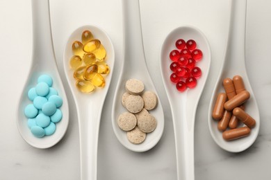 Photo of Spoons with different dietary supplements on white table, flat lay