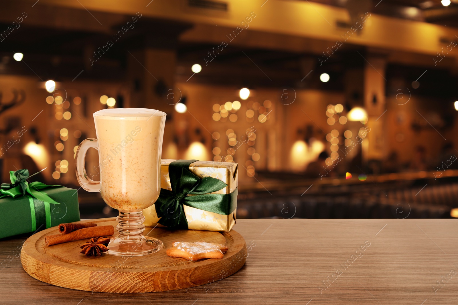 Image of Glass of delicious eggnog, spices, cookie and gift boxes on wooden table in bar, space for text