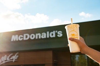 Photo of WARSAW, POLAND - SEPTEMBER 16, 2022: Woman holding cold McDonald's drink near restaurant outdoors, closeup