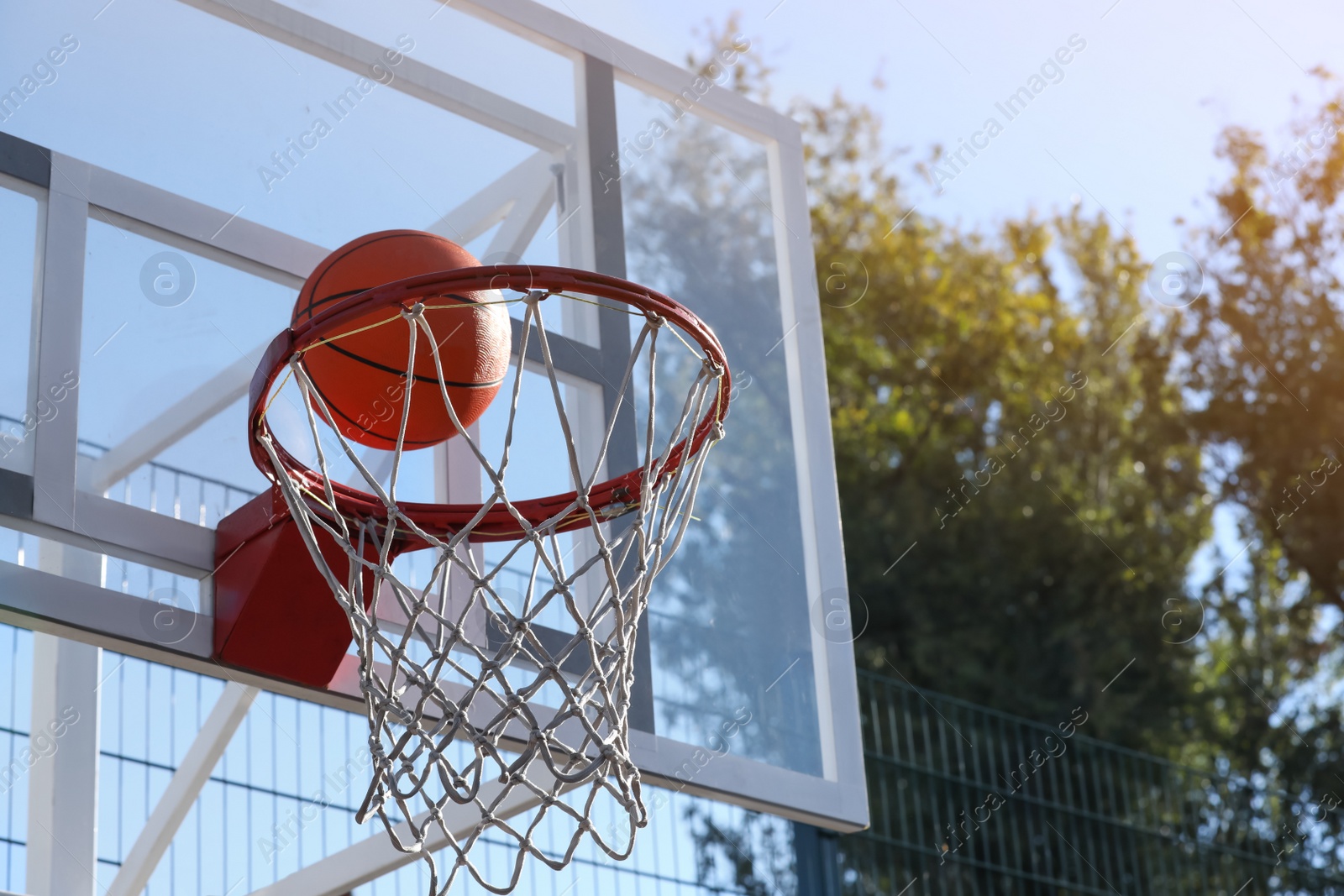 Photo of Basketball ball and hoop with net outdoors on sunny day