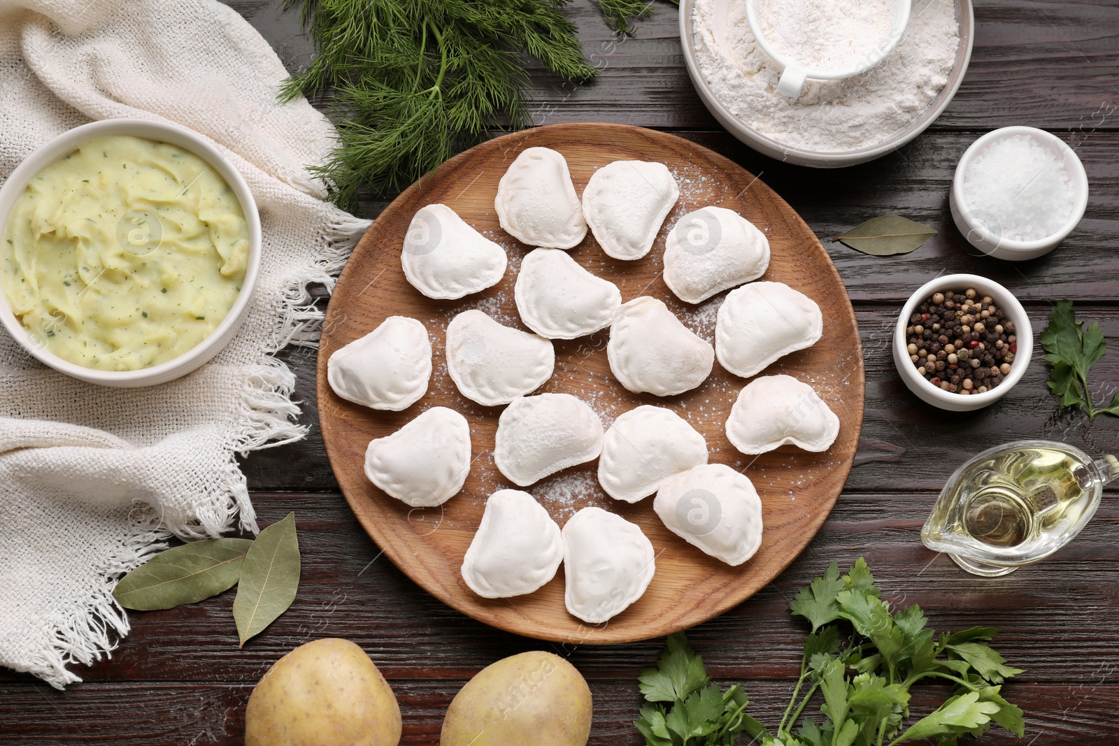 Photo of Raw dumplings (varenyky) and ingredients on brown wooden table, flat lay