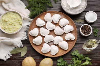 Raw dumplings (varenyky) and ingredients on brown wooden table, flat lay