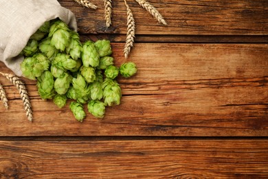 Photo of Sack with fresh green hops and wheat ears on wooden table, flat lay. Space for text