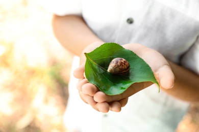 Photo of Boy playing with cute snail outdoors, closeup. Child spending time in nature