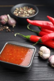 Photo of Spicy chili sauce, garlic, peppers and peppercorns on black wooden table, closeup