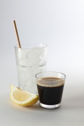 Photo of Coffee and ice cubes in different glasses, cut lemon on white background