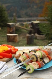 Metal skewers with raw marinated meat and vegetables on wooden table outdoors