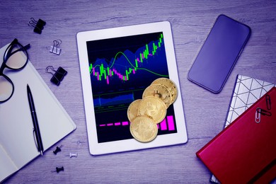 Image of Bitcoins, tablet with trading information and stationery on wooden table, flat lay