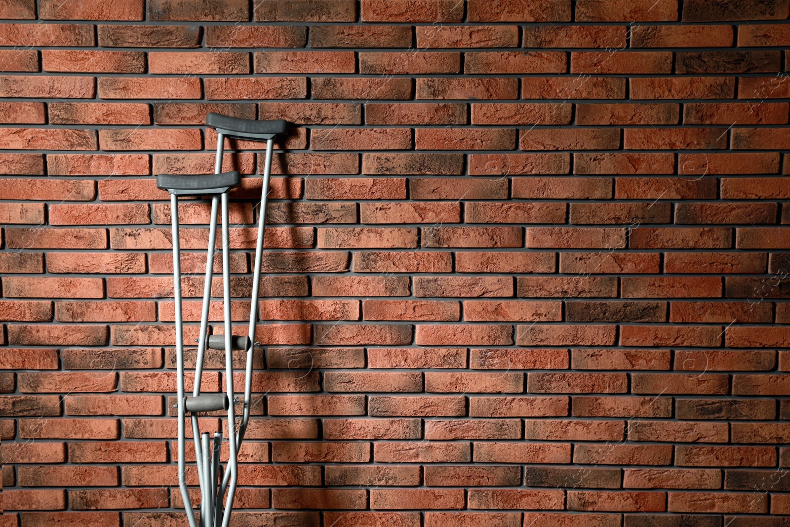 Photo of Pair of axillary crutches near red brick wall. Space for text