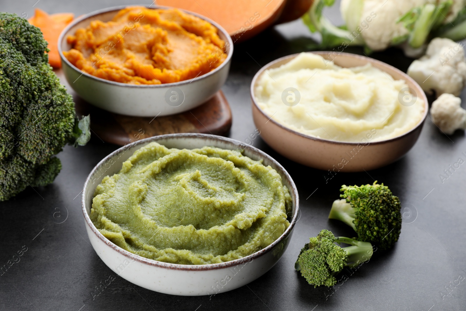 Photo of Bowls with tasty different puree and ingredients on black table, closeup