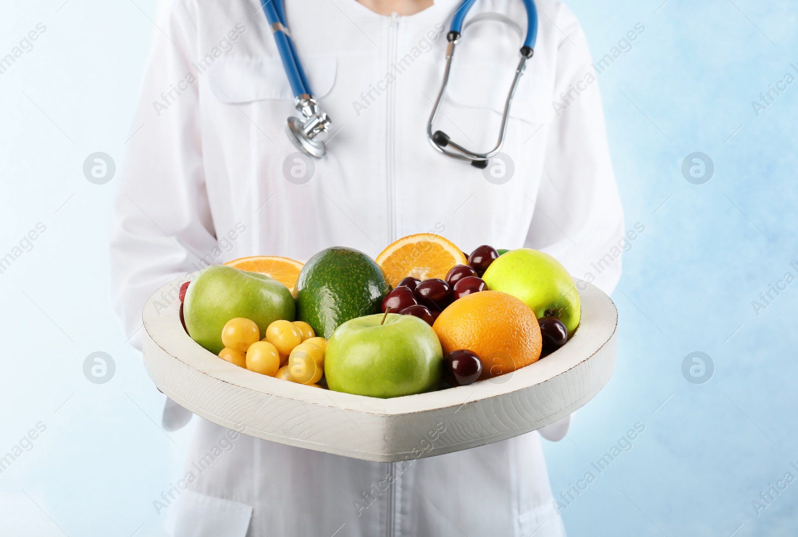 Photo of Female doctor holding plate with fresh fruits on light background. Cardiac diet
