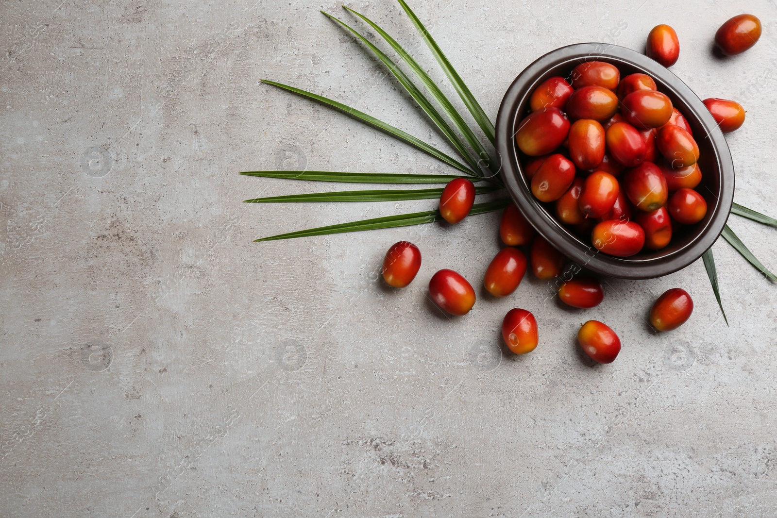 Photo of Palm oil fruits in bowl on grey table, flat lay. Space for text