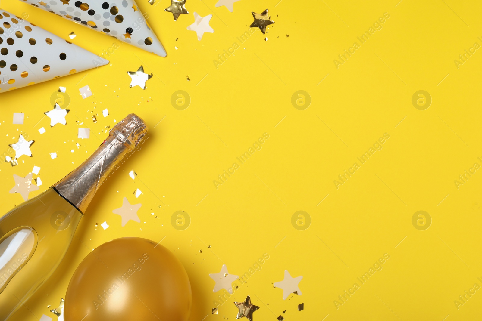 Photo of Flat lay composition with birthday decor and bottle of sparkling wine on yellow background, space for text