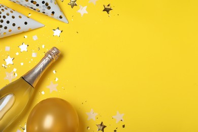 Flat lay composition with birthday decor and bottle of sparkling wine on yellow background, space for text