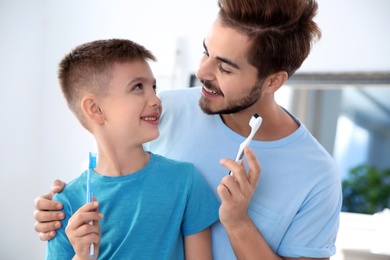 Photo of Young man and his son with toothbrushes in bathroom. Personal hygiene