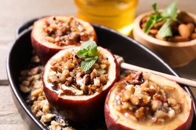 Tasty baked apples with nuts, honey and mint in baking dish on table, closeup