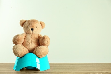 Photo of Teddy bear with blue potty on wooden table against light background, space for text. Toilet training