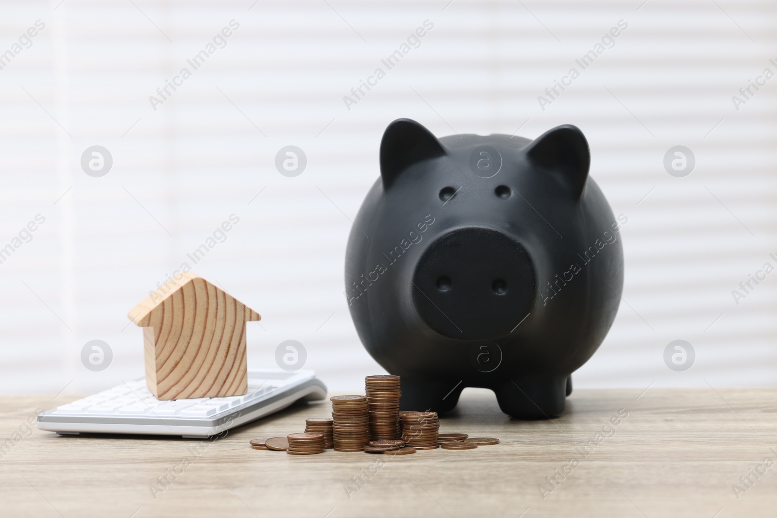 Photo of House model, calculator, piggy bank and stacked coins on wooden table