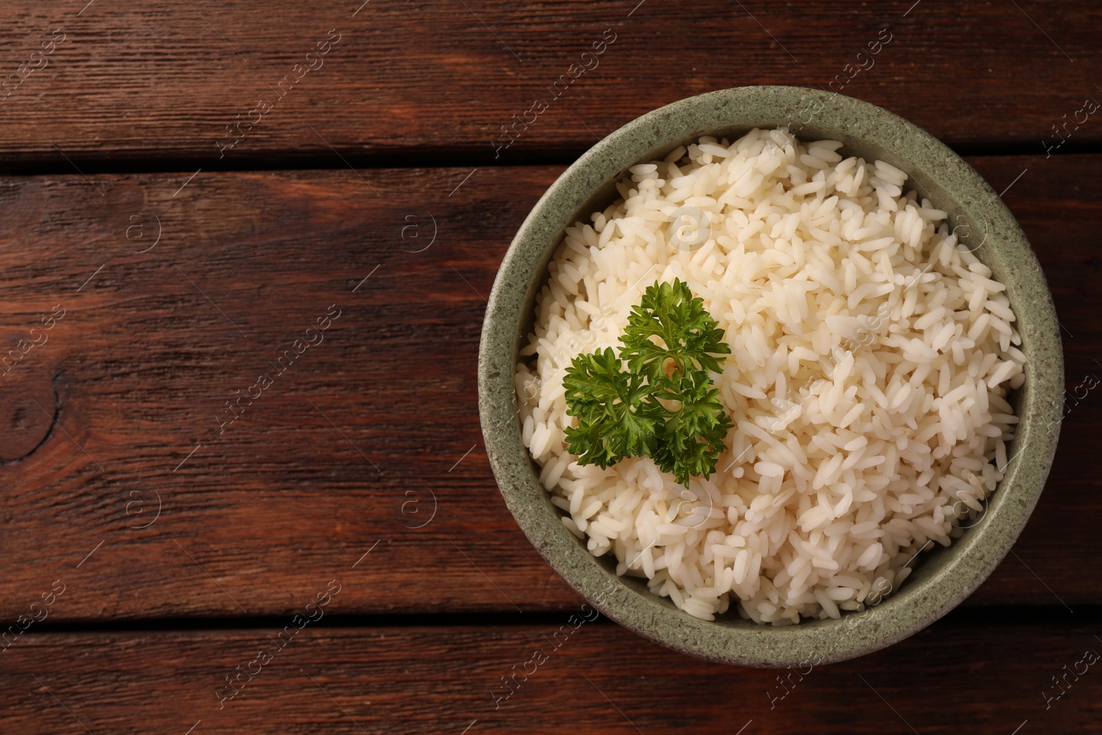 Photo of Delicious rice with parsley in bowl on wooden table, top view. Space for text