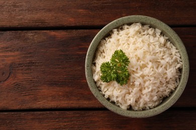 Delicious rice with parsley in bowl on wooden table, top view. Space for text