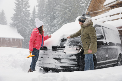 Photo of Young couple cleaning snow from car outdoors on winter day