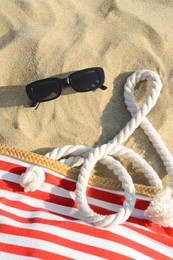 Stylish sunglasses and beach bag on sand, flat lay