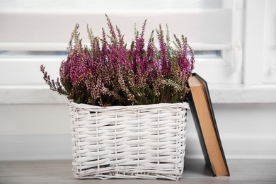 Photo of Beautiful heather flowers in wicker basket and book on table indoors