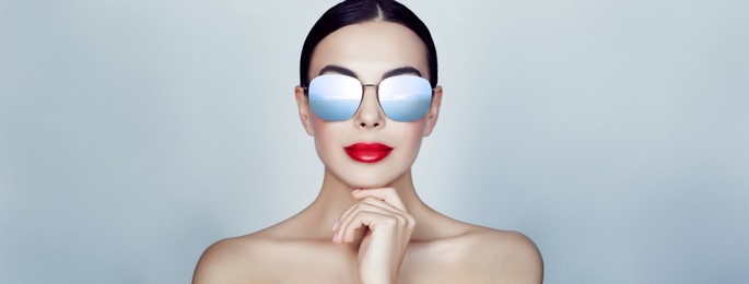 Image of Attractive woman in stylish sunglasses on light grey background, banner design. Sky with clouds reflecting in lenses