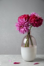 Photo of Beautiful dahlia flowers in vase on table against grey background