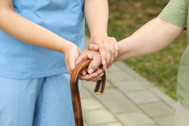 Elderly woman with walking cane and female caregiver outdoors, closeup