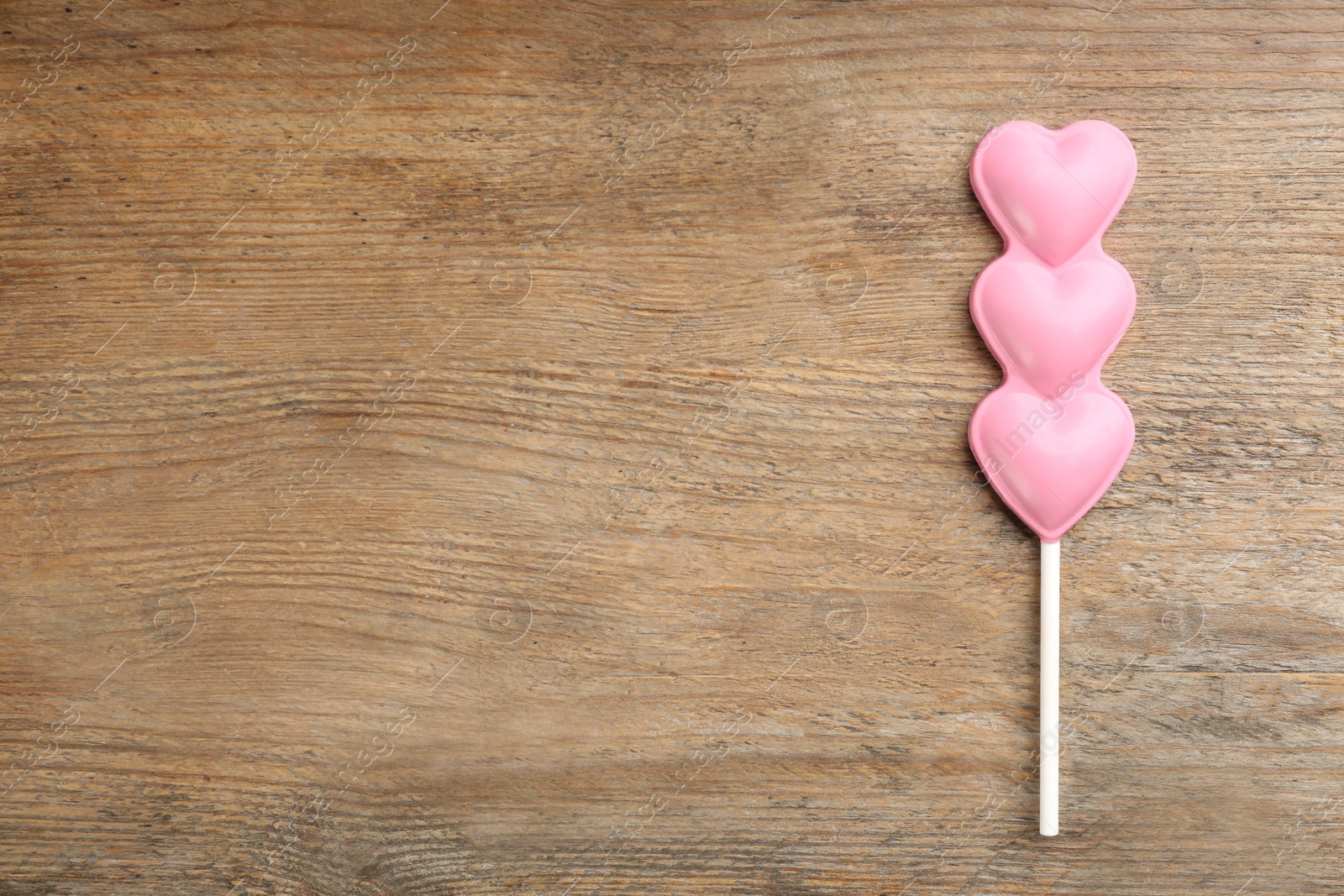 Photo of Chocolate heart shaped lollipop on wooden table, top view. Space for text