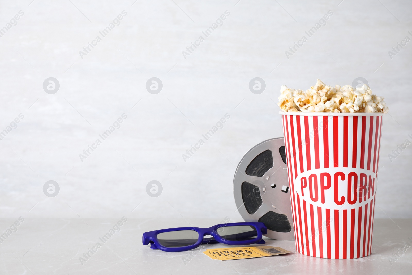 Photo of Delicious popcorn, glasses, ticket and tape on light table. Space for text