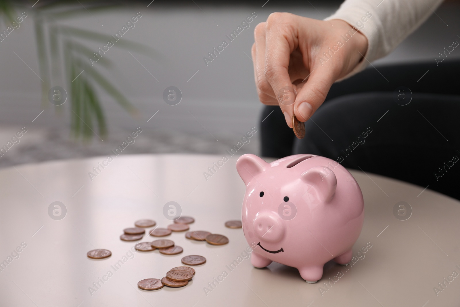 Photo of Woman putting money into piggy bank at table, closeup. Space for text