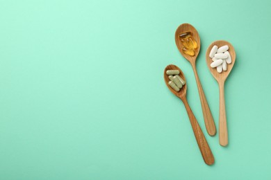 Photo of Different vitamin capsules in spoons on turquoise background, flat lay. Space for text