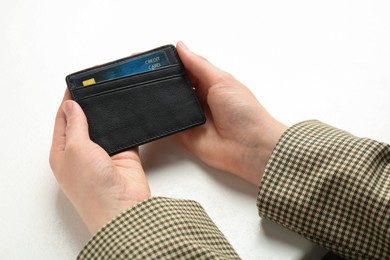 Woman holding leather card holder with credit card at white table, closeup