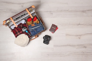 Suitcase with clothes, passports and camera on wooden background, top view with space for text. Winter vacation