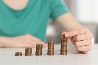 Photo of Financial savings. Woman stacking coins at white wooden table, closeup