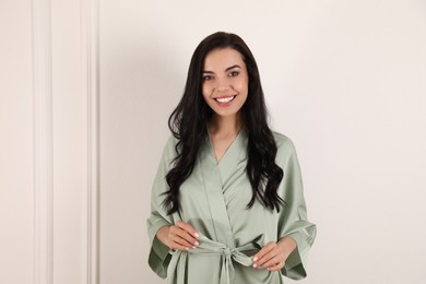 Pretty young woman in beautiful light silk robe near white wall