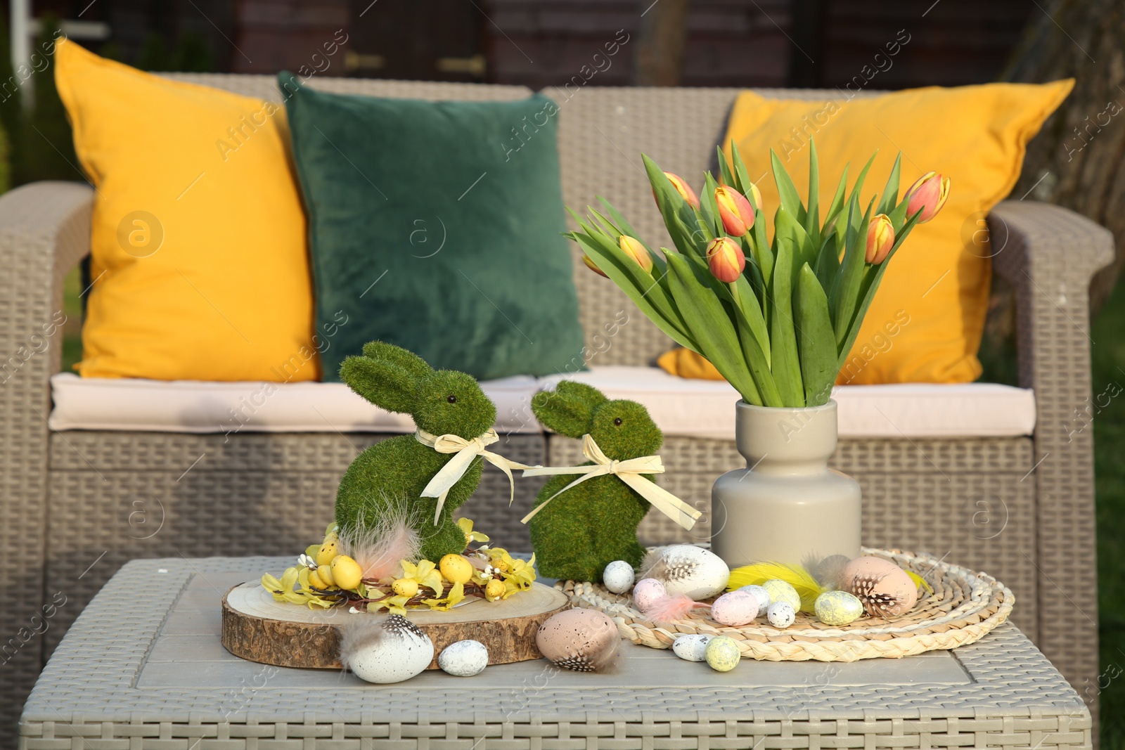 Photo of Terrace with Easter decorations. Bouquet of tulips in vase, bunny figures and decorative eggs on table outdoors