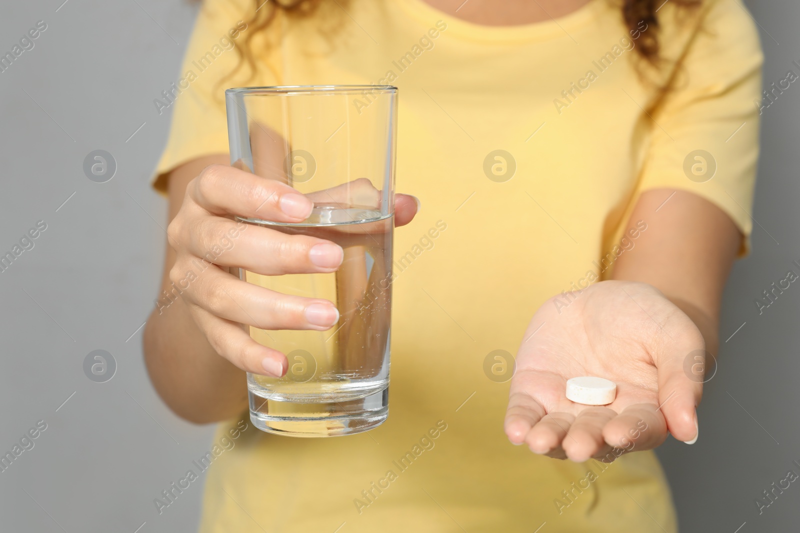 Photo of African-American woman with glass of water and vitamin pill on light grey background, closeup