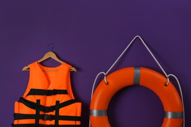 Photo of Orange life jacket and lifebuoy on violet background. Rescue equipment