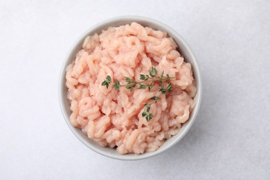 Photo of Fresh raw minced meat and thyme in bowl on light grey table, top view