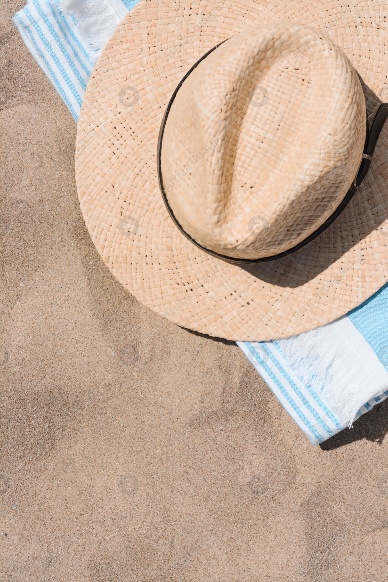 Photo of Straw hat and beach towel on sand, top view. Space for text