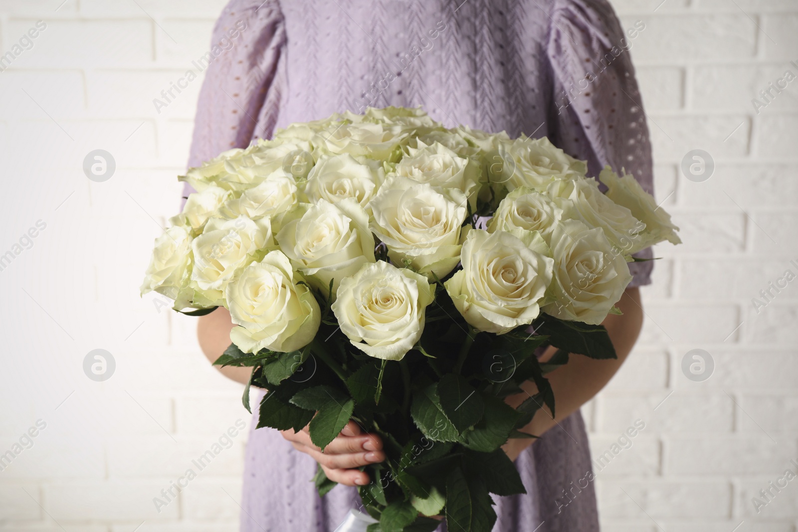 Photo of Woman holding luxury bouquet of fresh roses near white brick wall, closeup