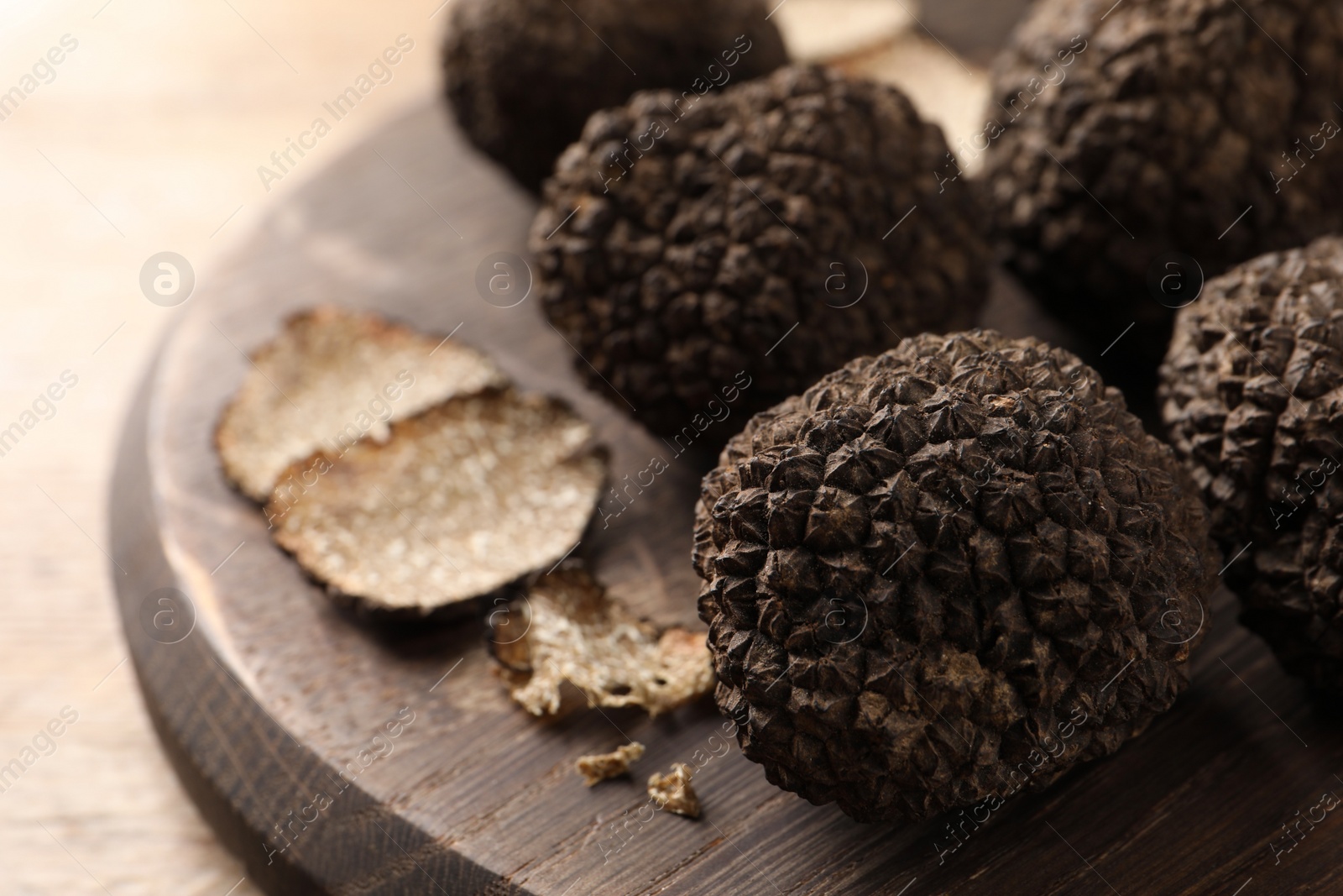 Photo of Whole and cut black truffles with wooden board on table, closeup