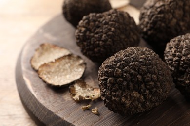 Whole and cut black truffles with wooden board on table, closeup