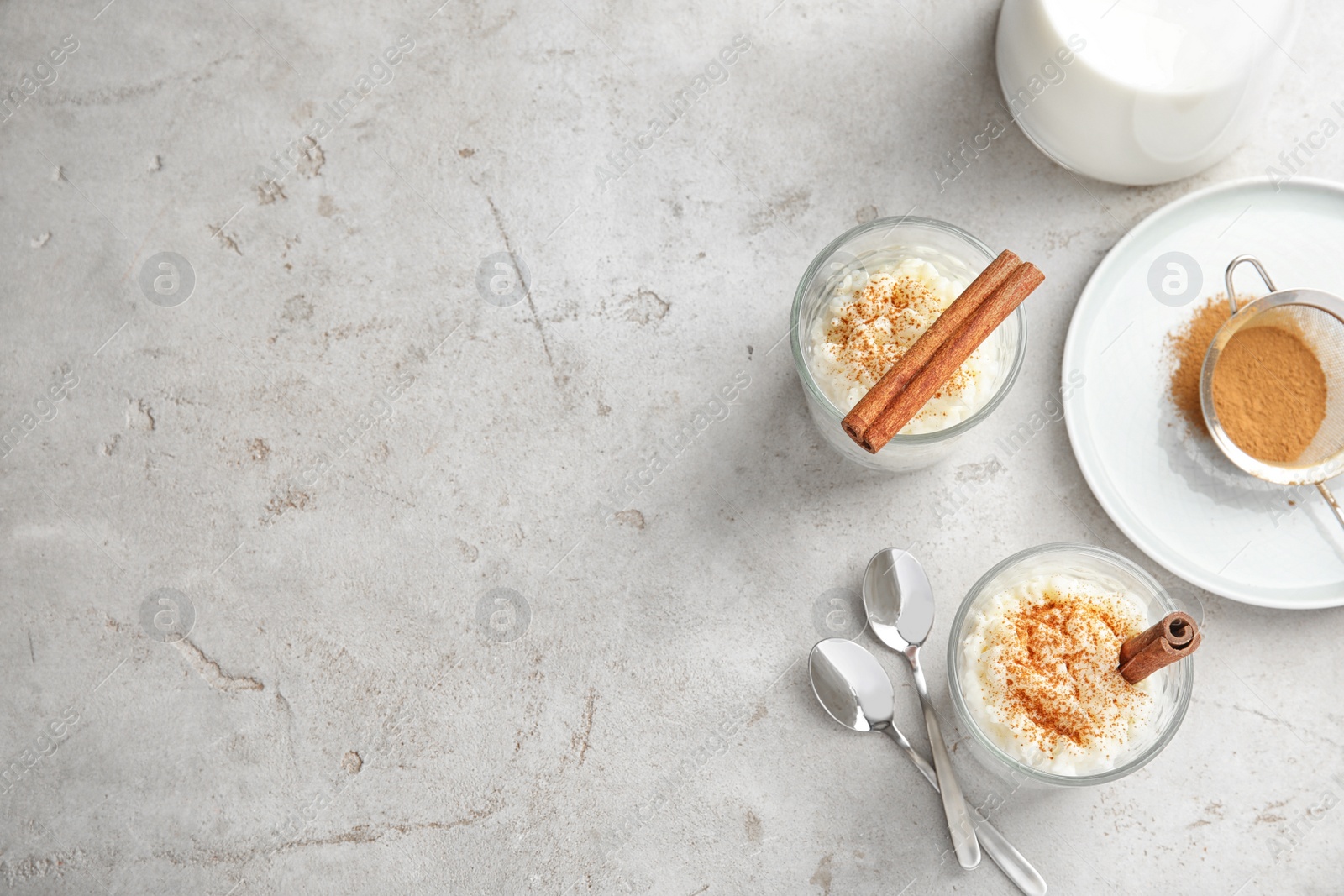 Photo of Creamy rice pudding with cinnamon in glasses served on grey table, top view. Space for text