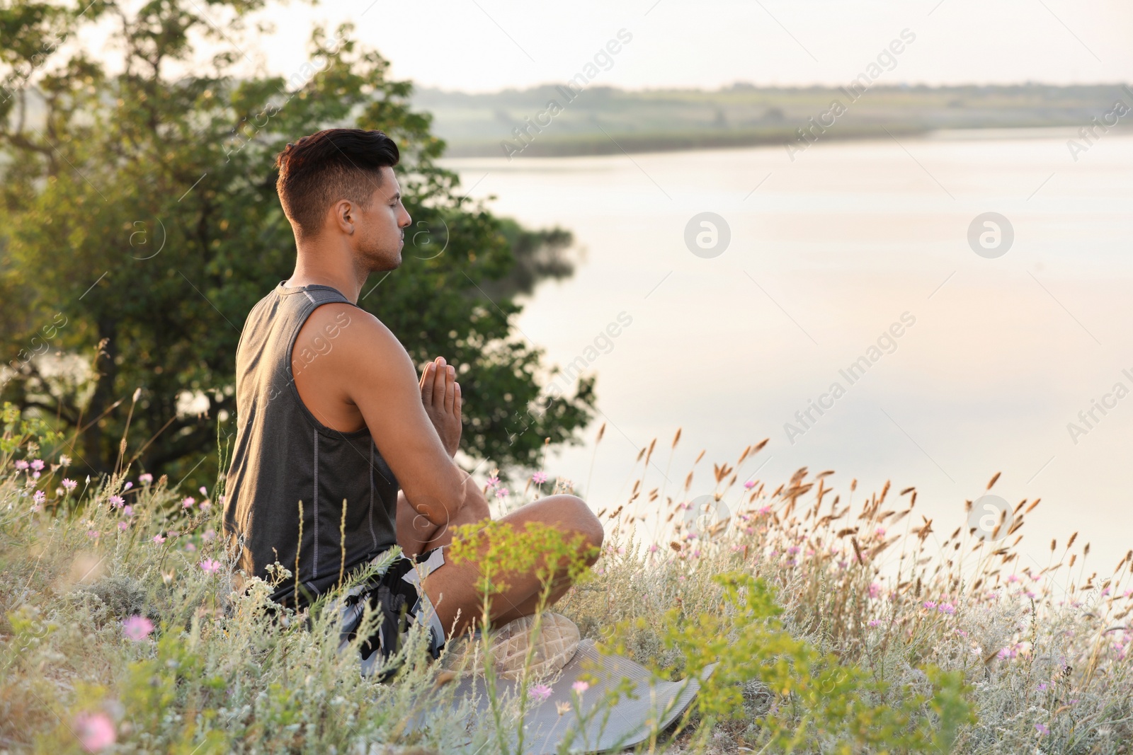 Photo of Man meditating in meadow near river. Space for text