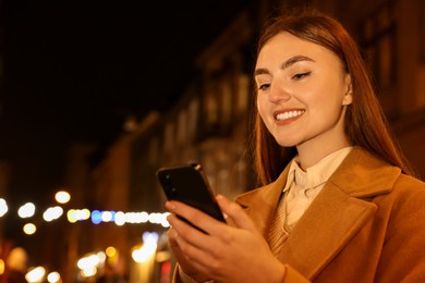 Smiling woman using smartphone on night city street. Space for text