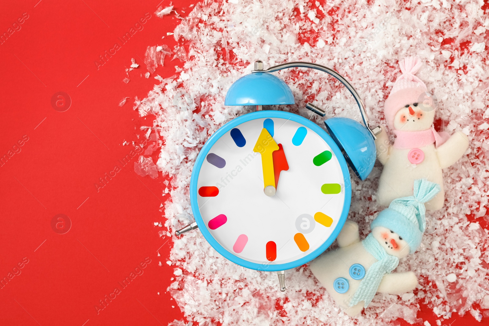 Photo of Alarm clock and snowmen in pile of snow on red background, flat lay with space for text. New Year countdown